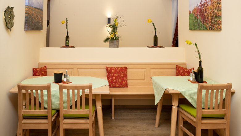 Breakfast room, © Nadine Beles A cozy breakfast room with wooden furniture, green tablecloths and yellow flowers in bottle vases. Landscape paintings hang on the walls.