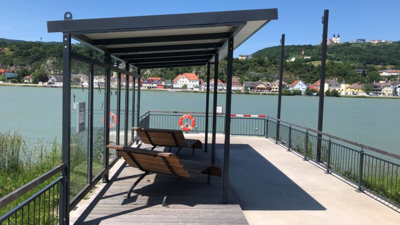 Krummnussbaum landing stage opposite the Maria Taferl basilica, © Donau NÖ Tourismus Landing stage with benches by the river, a town and a basilica on a hill in the background.