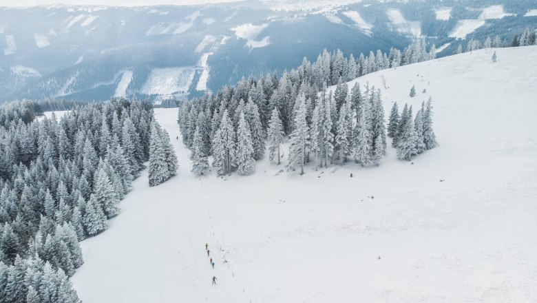 Change panorama trail, © DJI_0557 Snow-covered landscape with cross-country skiers on a trail, surrounded by snow-covered trees and mountains in the background.