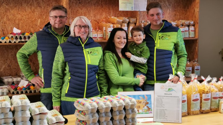 he family stands behind a counter selling eggs and pasta., © Familie List A family in green clothing stands behind a counter selling eggs and pasta.
