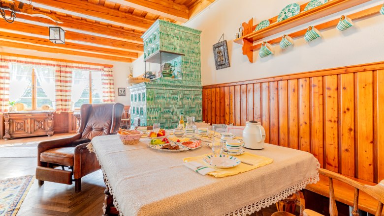 Woltron Manor, © Wiener Alpen / Christian Kremsl Cozy dining room with wooden furniture, set table and green tiled stove.