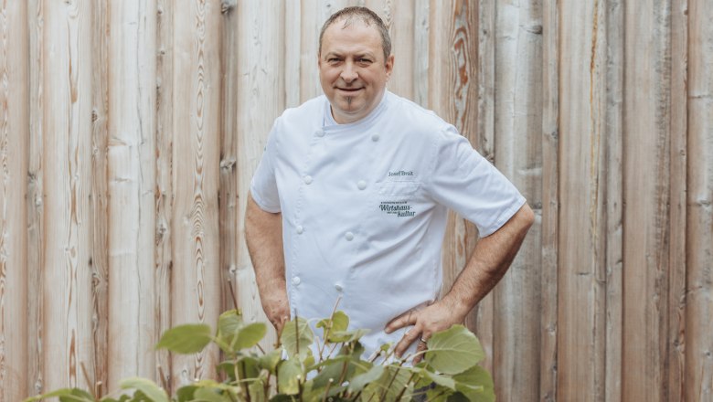 Landlord Josef Brait, © Niederösterreich Werbung/David Schreiber A man in a white chef's jacket stands in front of a wooden wall.