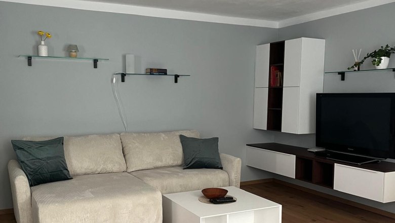 Living space, © Jochen Maurer Modern living room with beige couch, white coffee table, wooden floor and wall shelves.