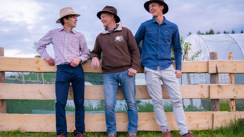 The market gardeners, © Michaela Faustmann Fotografie Three men in hats lean against a wooden fence in a meadow, smiling.