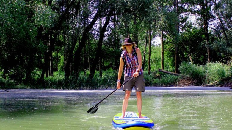 Stand up paddling, © www.standuppaddeln.at Person stand up paddling on a river, surrounded by trees.
