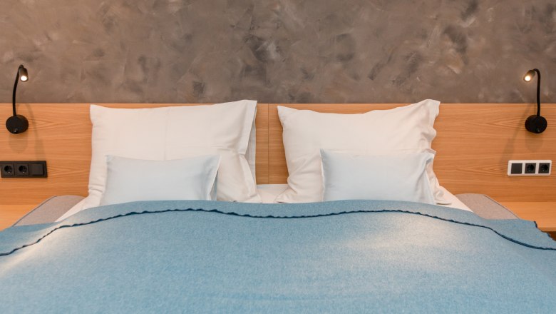 House by the lake, © schwarz-koenig.at A double bed with a blue blanket and white pillows in front of a gray wall.