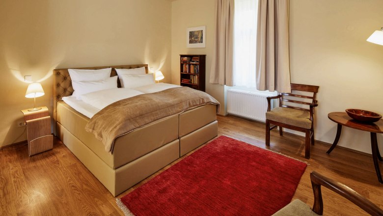 Villa Tranquillini/Suite Emma, © Herbert Lehman A cozy bedroom with a large bed, two bedside tables with lamps, a red carpet and wooden furniture.