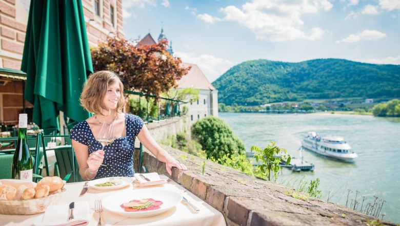 Restaurant terrace, © Florian Schulte Woman enjoying wine on restaurant terrace with river view.