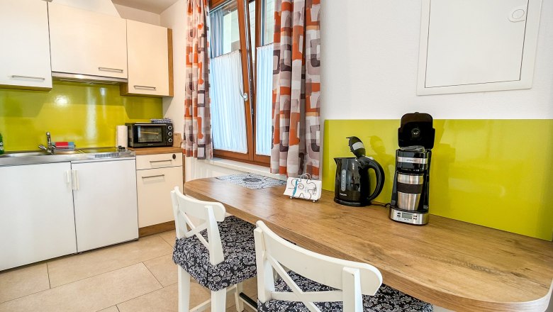 House Morgensonne Kitchen, © Fam. Pauker Modern kitchen with green splashback, white cupboards, wooden counter and coffee machine.