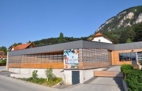 Mohr-Sederl Fruit World, © Mohr-Sederl Fruchtwelt Modern building with wooden cladding and advertising sign for Mohr-Sederl Fruchtwelt, surrounded by green countryside and mountains.