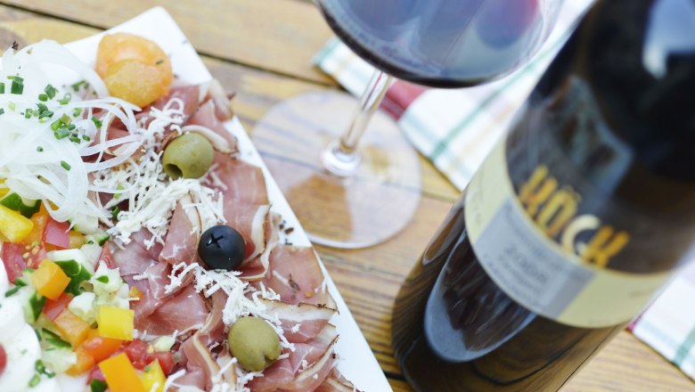 Wine tavern specialties, © Steve Haider A plate of ham, olives, vegetables and a glass of red wine on a wooden table.