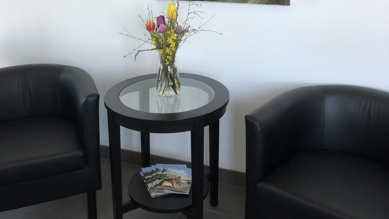 Amber Motel, © Bernstein Motel Two black armchairs and a round table with flowers in a room. An abstract painting with a fox motif hangs on the wall.