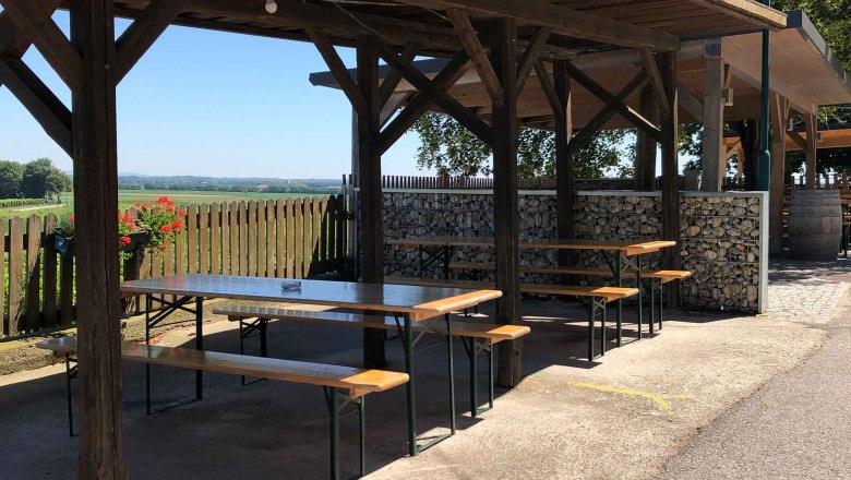 Denk wine tavern, © Donau Niederösterreich Covered outdoor area with wooden benches and tables, surrounded by nature.