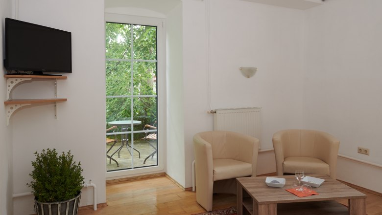 Living area, © Landhaus Puchbergerhof by smc Living room with two beige armchairs, wooden table, TV and balcony with table and chairs.