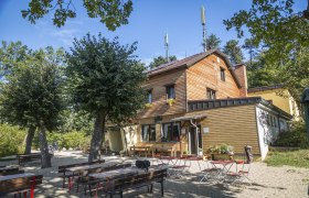 Viewpoint Waxeneckhaus, © Wiener Alpen, Foto: Franz Zwickl Wooden house with outdoor beer garden surrounded by trees.
