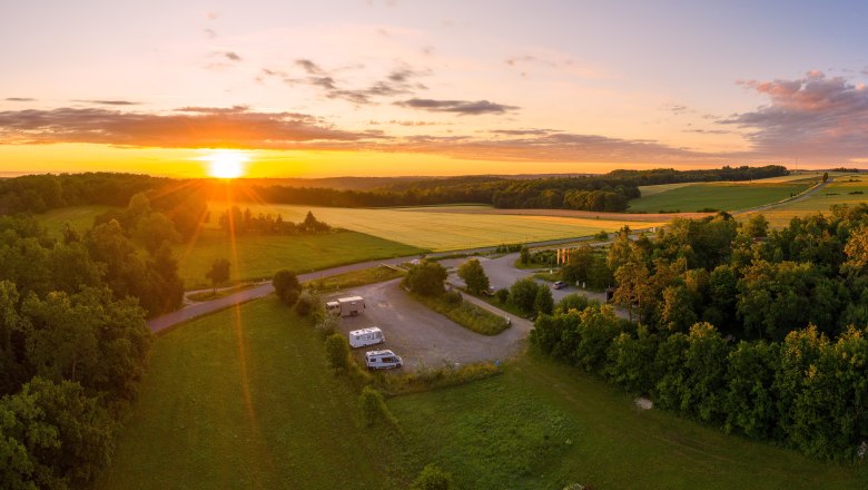 Motorhome parking space, © Kiesling Aerial view of a motorhome site at sunset, surrounded by fields and woods.