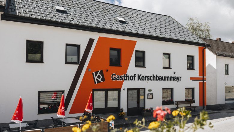 Inn with bakery and adjoining coffee house, © Niederösterreich Werbung/David Schreiber Exterior view of the Gasthof Kerschbaummayr with orange façade and red parasols.