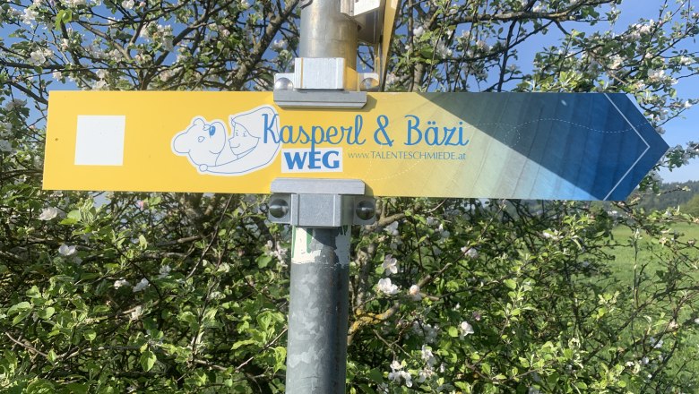 Family hiking trail, © Sabine Kerschbaumer Signpost with the inscription 'Kasperl & Bäzi WEG' in front of a blossoming tree.