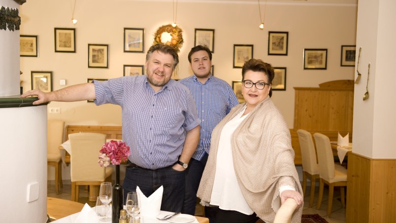 nik_3521a, © Donauwirt / Nik Pichler The host family in a restaurant, smiling and looking at the camera. The room is decorated with pictures and a wreath.