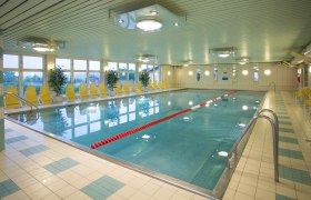 Swimming pool, © Benjamin Wald Interior view of an empty indoor pool with yellow deckchairs and plants.