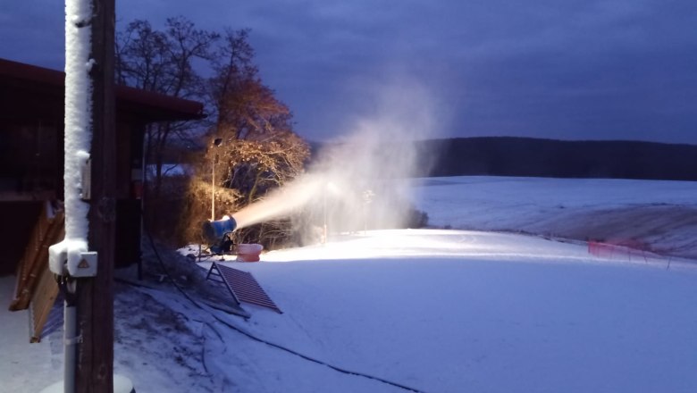 Snowmaking on the piste, © Fritz Weiss Snow cannon makes snow on a slope at dusk.