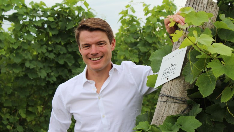 Roman Josef Pfaffl, © Weingut R&A Pfaffl A man in a vineyard next to a sign with the inscription 'Weingut Pfaffl'.