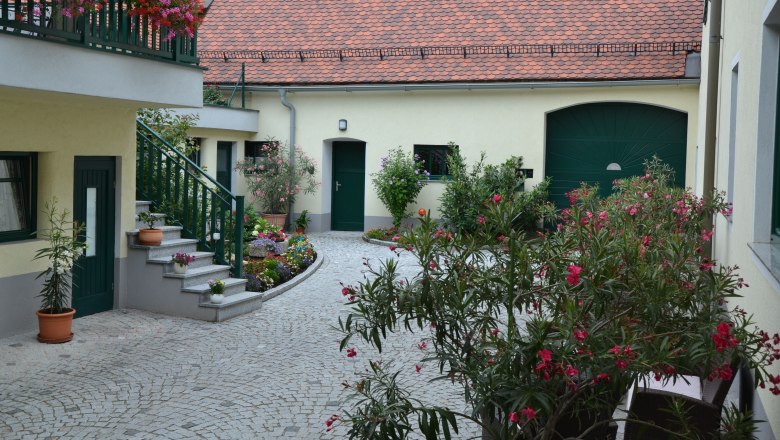 Winery Krottendorfer, © Familie Krottendorfer A well-tended courtyard with flowers and plants, surrounded by buildings with red tiled roofs and green doors.