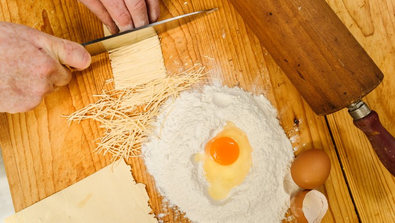 Emperor of Austria, © Rita Newman Close-up of hands cutting pasta dough, with flour, egg and rolling pin on a wooden table.