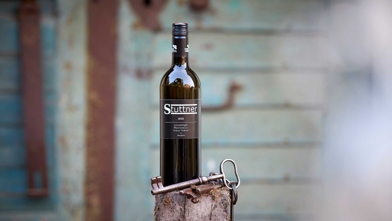 Wine bottle, © Weinbau Stuttner A Stuttner wine bottle stands on a tree stump with old keys in front of a blurred, rustic background.