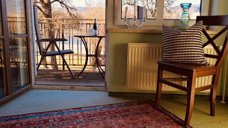 Rooms in the main building, © Szilágyi A room with carpet, chair and view of a balcony with table and chairs, trees in the background.