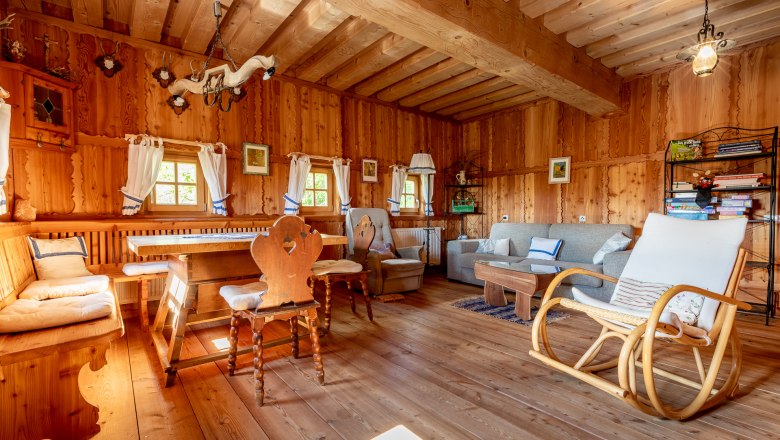 Dining area, © Wiener Alpen / Christian Kremsl Dining area with wooden furniture, rocking chair and sofa in a room with wood paneling.