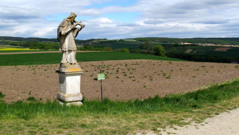 Nepomuk statue in Baierdorf, © Marktgemeinde Ravelsbach Statue of Nepomuk in a field in Baierdorf, surrounded by a green landscape and a cloudy sky.