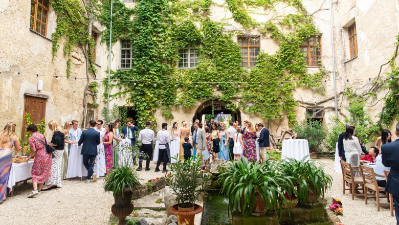 Inner courtyard, © weddings by avocadi People gather in a leafy courtyard with tables and decorations.
