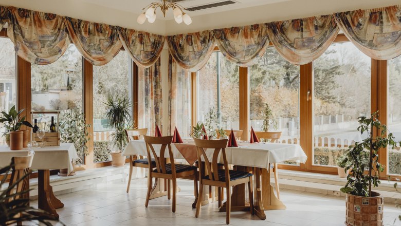 A bright restaurant with large windows, wooden furniture and plants.