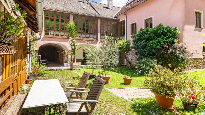 Inner courtyard with garden furniture, plants and pink building in the background.
