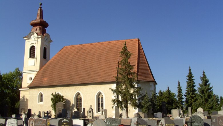 Exterior view of a church with a cemetery in the foreground and a blue sky.