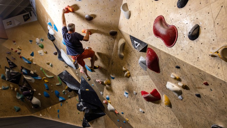 Person bouldering on a climbing wall with colorful holds.