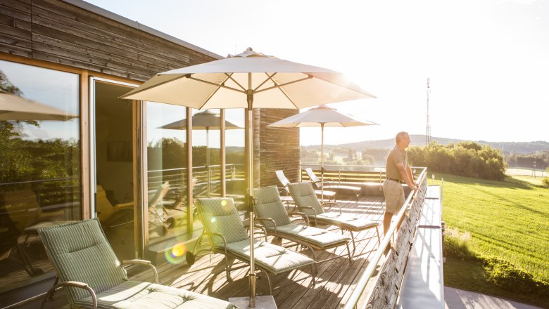 Sunny roof terrace with sun loungers and parasols, with a view of the countryside.