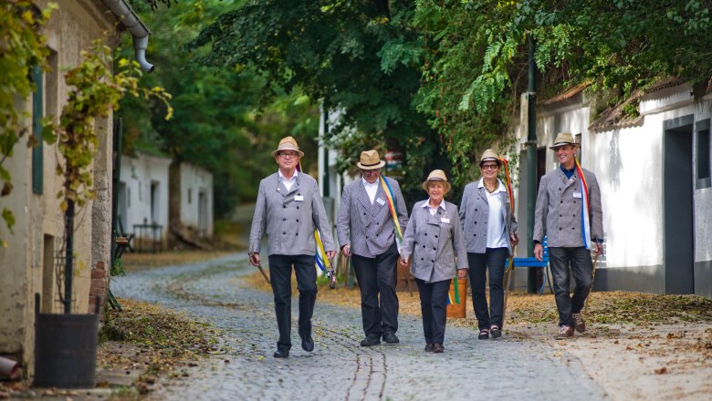 Five people in traditional dress walk along a cobbled street.