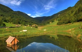 A small pond in a green mountain landscape with a blue sky.