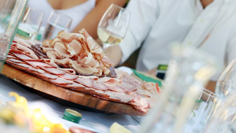 A table with a platter full of cold cuts and glasses of white wine.