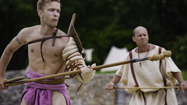 Two men in gladiator costumes with spears outdoors.