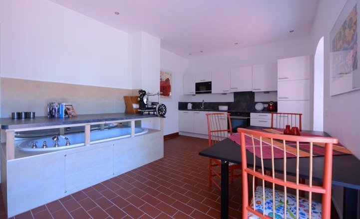 Modern kitchen with white cupboards, dining table and red chairs.