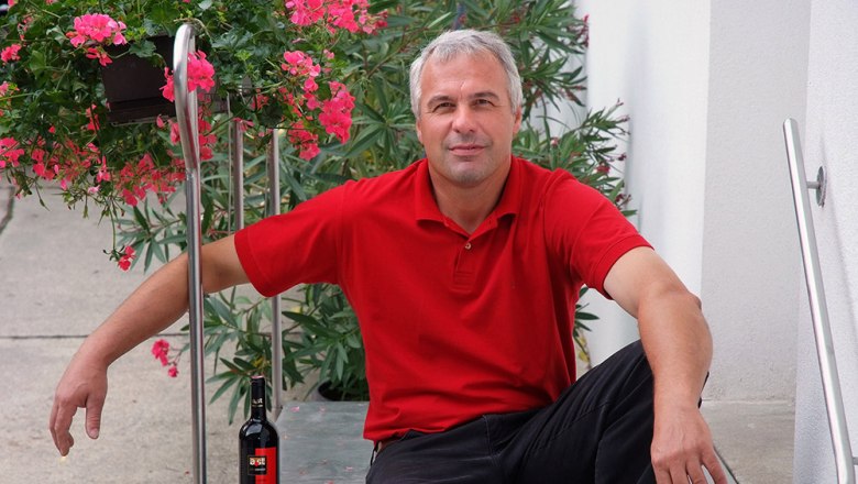 A man in a red shirt sits on a staircase next to a bottle of wine and flowers.