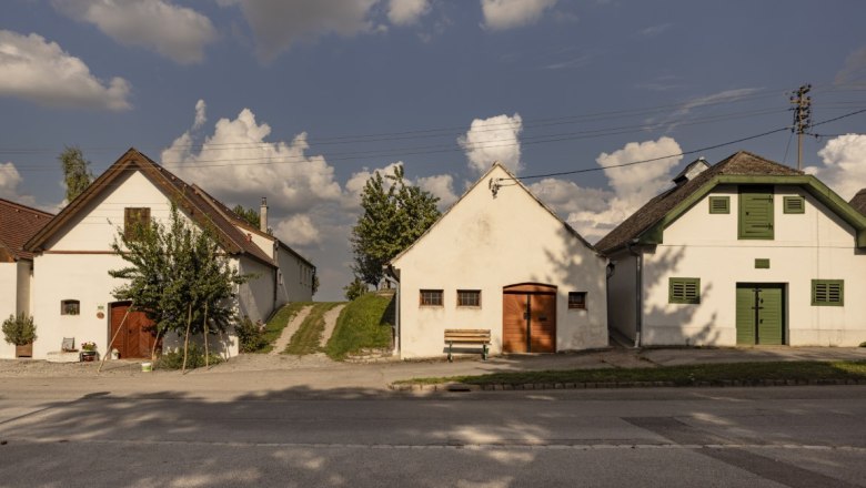 Three traditional cellar houses in Kettlasbrunn under a blue sky with clouds.
