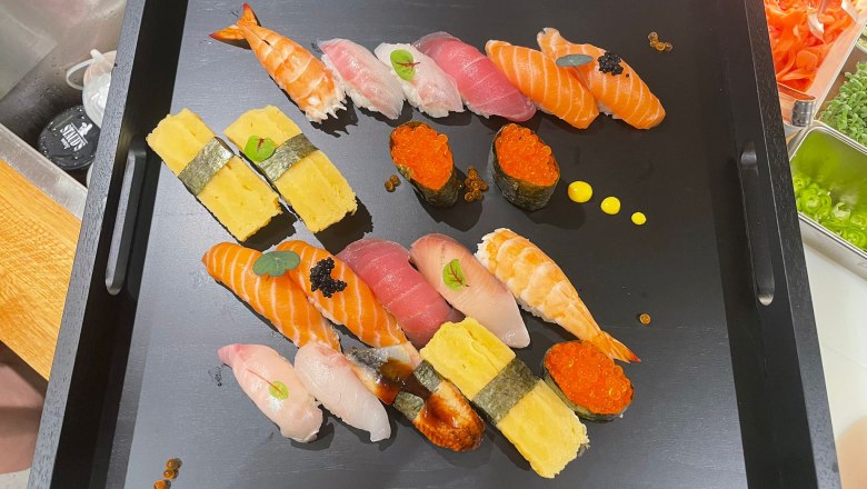 A black tray with a selection of sushi, including nigiri and maki, decorated with caviar and herbs.