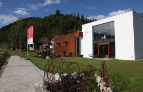 Modern gallery with glass façade and rusty metal sculptures in a green setting.