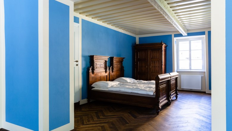 A room with blue walls, a wooden bed and a wardrobe.