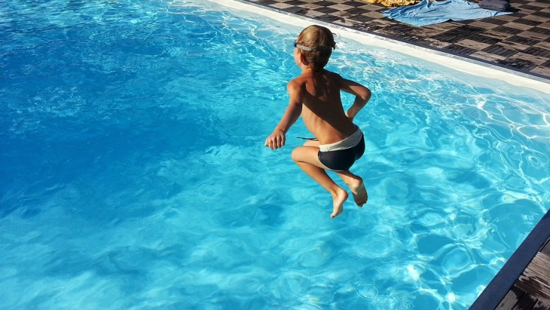 A child jumps into a pool of clear blue water.