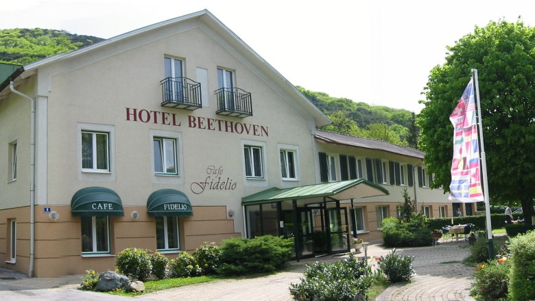 Exterior view of the Hotel Beethoven with Café Fidelio, surrounded by trees and flags.
